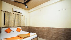A neatly made bed with orange bedding, a ceiling fan, and an air conditioning unit on the wall. - Hotel Sai Parikrama (Navi Mumbai)