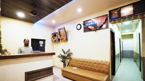 A reception area with a wooden reception desk, a brown sofa, and a potted plant. - Hotel Sai Parikrama (Navi Mumbai)