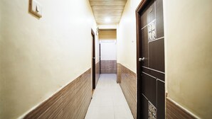 A narrow hallway with a tiled floor, a wooden door on the right, and a light switch on the left. - Hotel Sai Parikrama (Navi Mumbai)