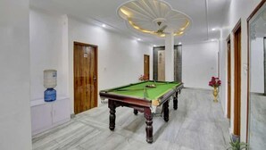 A pool table in a room with white walls, a wooden door, and a ceiling fan. - Hotel Grand (New Delhi)