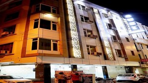 A multi-story building with illuminated signage, a ground-level entrance, and parked vehicles. - Hotel Grand (New Delhi)