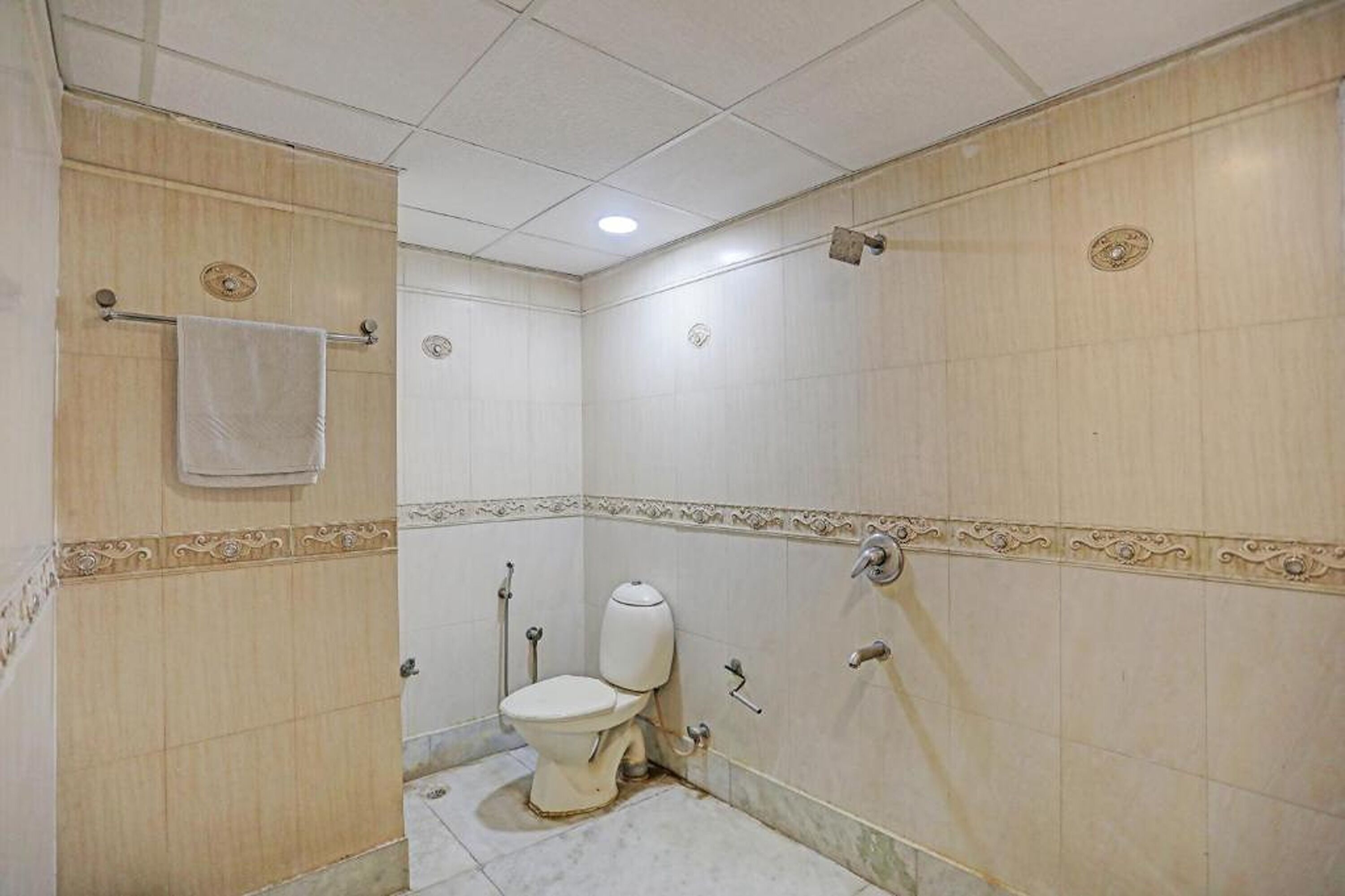 A small, tiled bathroom with a toilet, a towel rack, and a shower area.