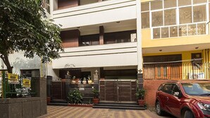 A multi-story building with a gated entrance, a red car parked in front, and a tiled pavement. - Greenleaf Apartment And Suites, Chittaranjan Park (New Delhi)