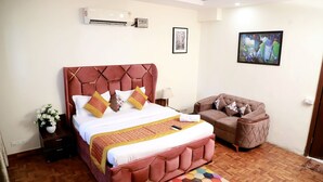 A bedroom with a large bed, a sofa, a nightstand with a vase of flowers, and a painting on the wall. - Greenleaf Apartment And Suites, Chittaranjan Park (New Delhi)