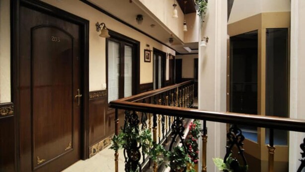 A hotel corridor with wooden doors, a staircase with a railing, and hanging plants. - Greenleaf Apartment And Suites, Chittaranjan Park (New Delhi)