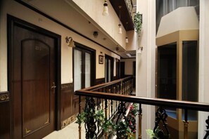 A hotel corridor with wooden doors, a staircase with a railing, and hanging plants. - Greenleaf Apartment And Suites, Chittaranjan Park (New Delhi)