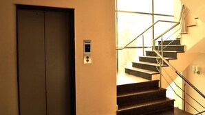 A modern interior with a staircase leading to a landing, a door, and a light switch on the wall. - Greenleaf Apartment And Suites, Chittaranjan Park (New Delhi)