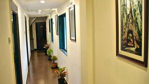 A long, narrow hallway with wooden flooring, flanked by walls with framed pictures and potted plants. - Silver Leef (Wai)