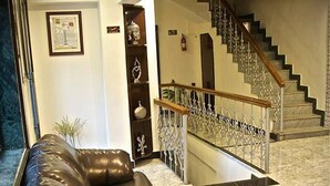 A living room with a brown leather sofa, a staircase with a wooden railing, and a marble floor. - Silver Leef (Wai)