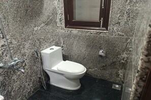 A bathroom with a white toilet, granite walls, and a small window. - Greenleaf Apartment And Suites, Kalkaji (New Delhi)