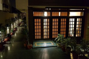 A corridor with potted plants, a wooden door with glass panels, and a tiled floor. - Greenleaf Apartment And Suites, Kalkaji (New Delhi)
