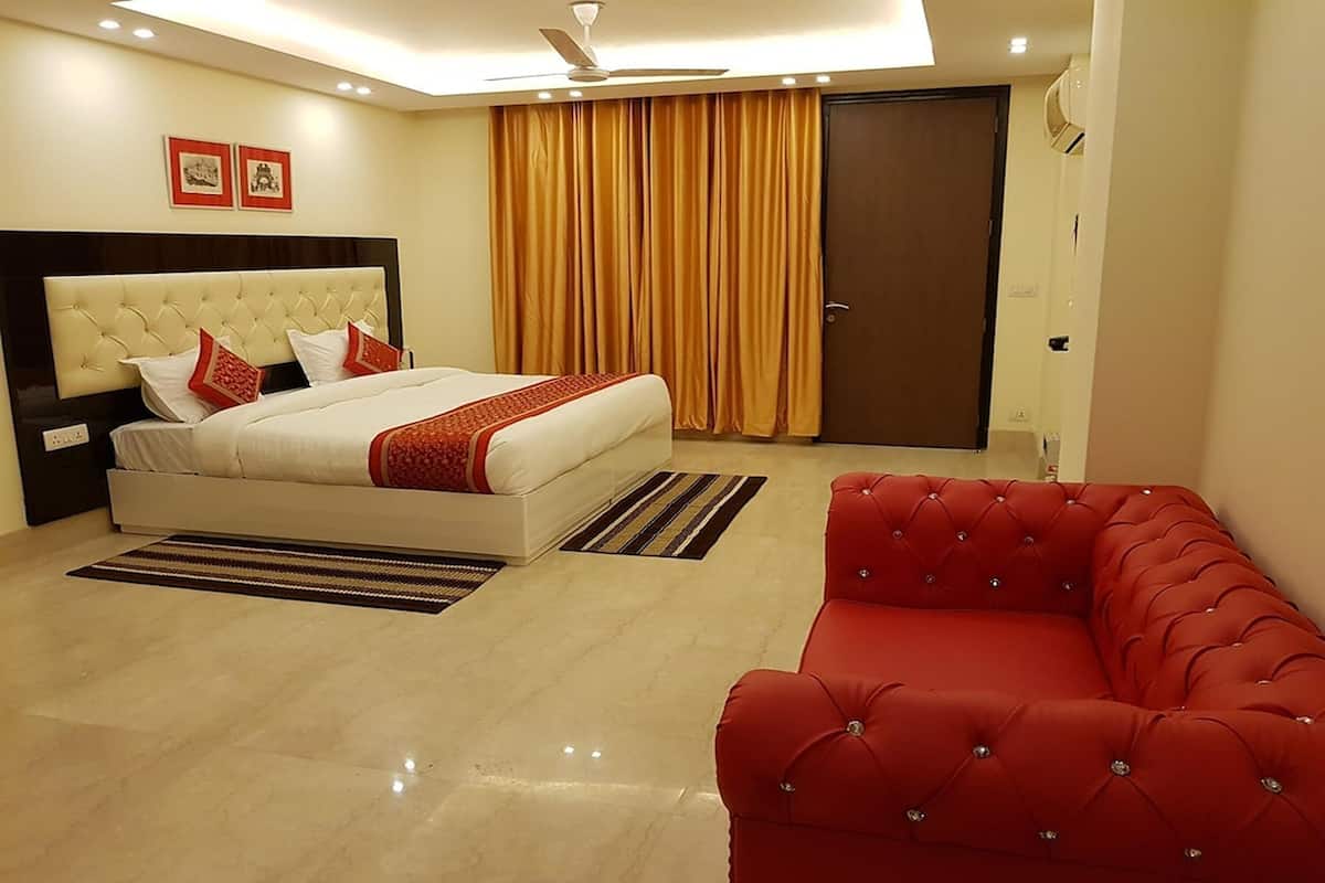 A bedroom with a bed, a red sofa, a ceiling fan, and a door.