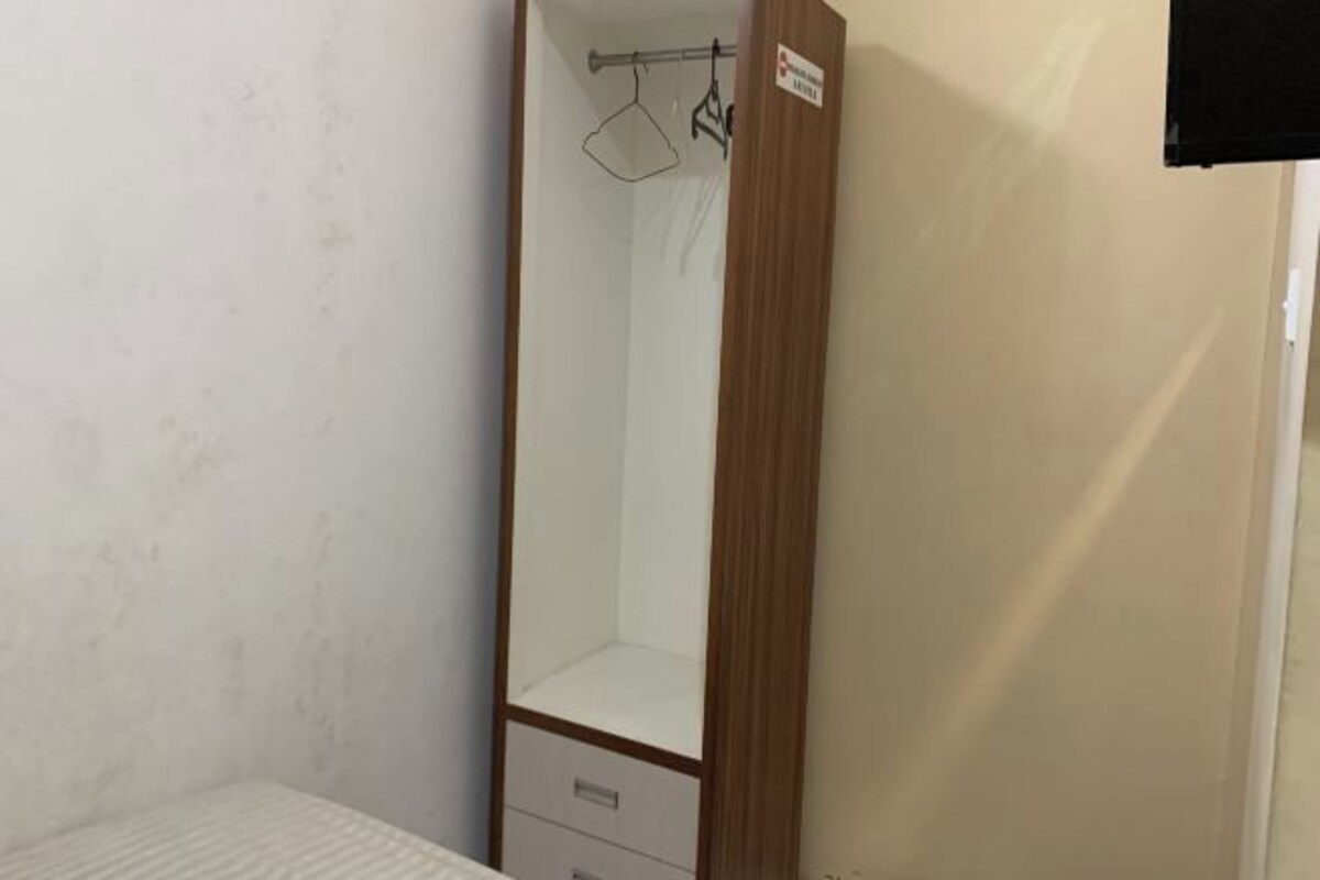 A bedroom with a wooden wardrobe, a hanging light fixture, and a white bed.