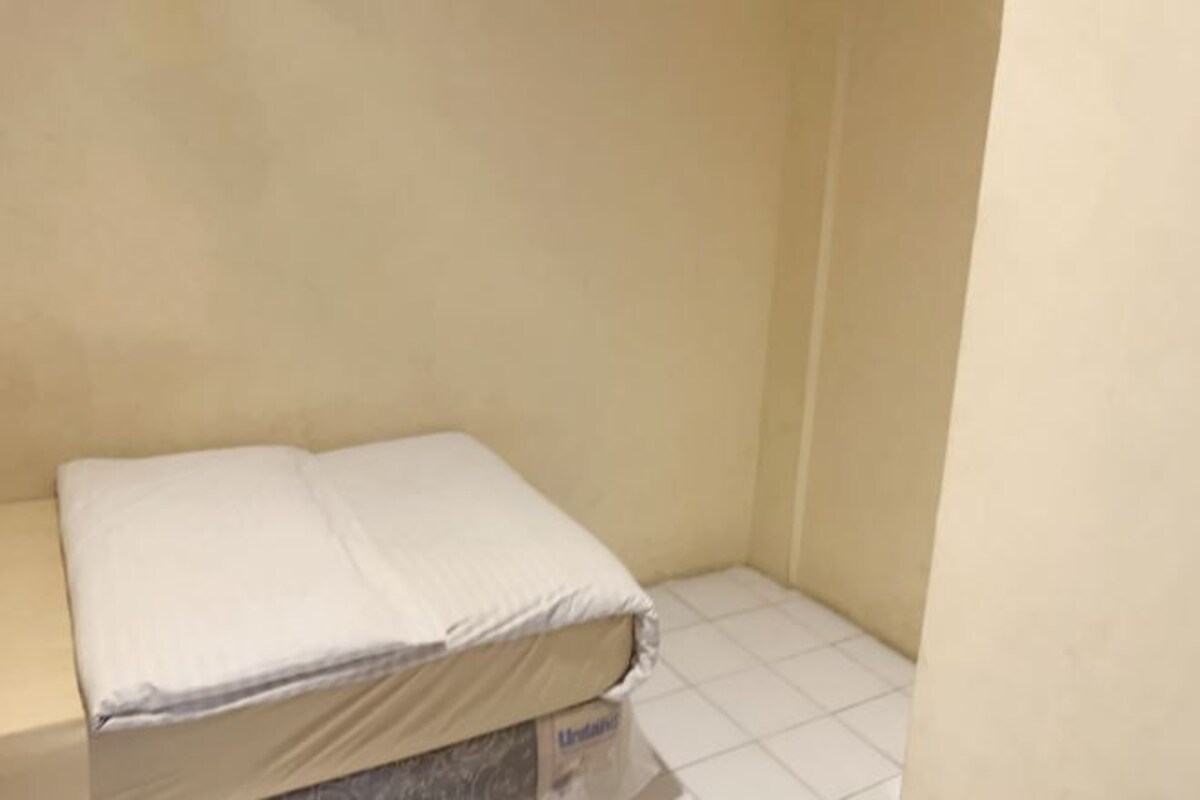 A small, unadorned room with a single bed and a tiled floor.