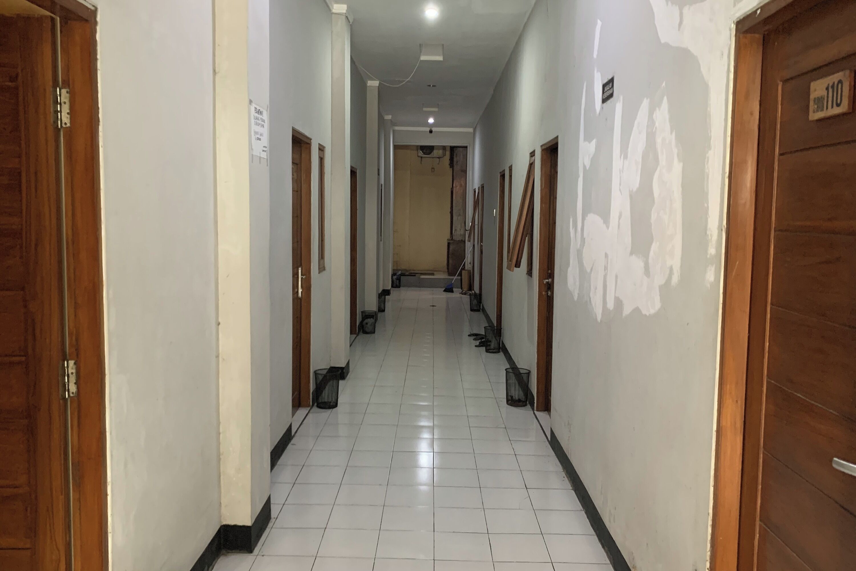 A hallway with white tiled floors, wooden doors, and a sign on the wall.