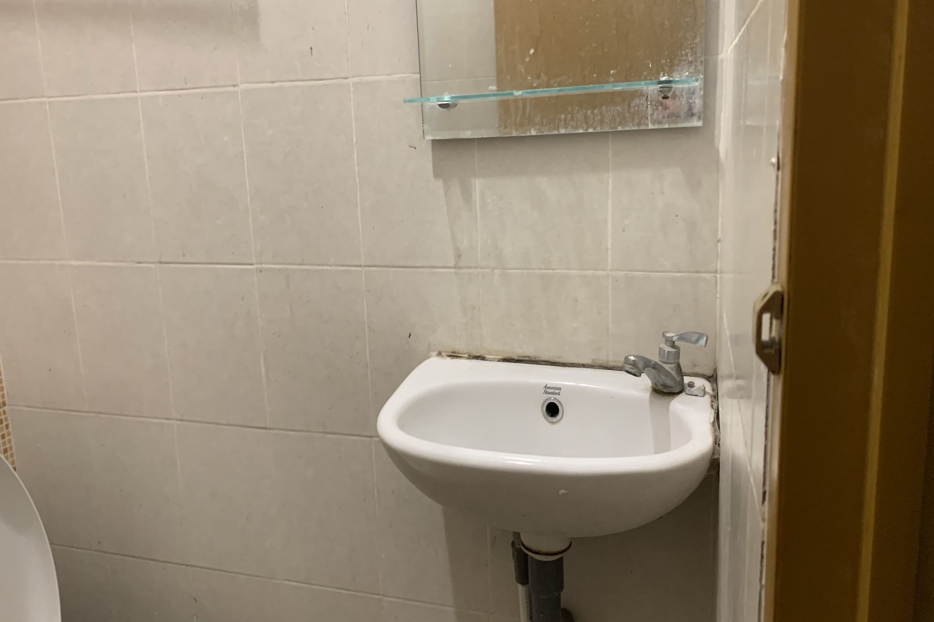 Un baño con un lavamanos blanco, un estante de vidrio encima y una puerta a la derecha.
