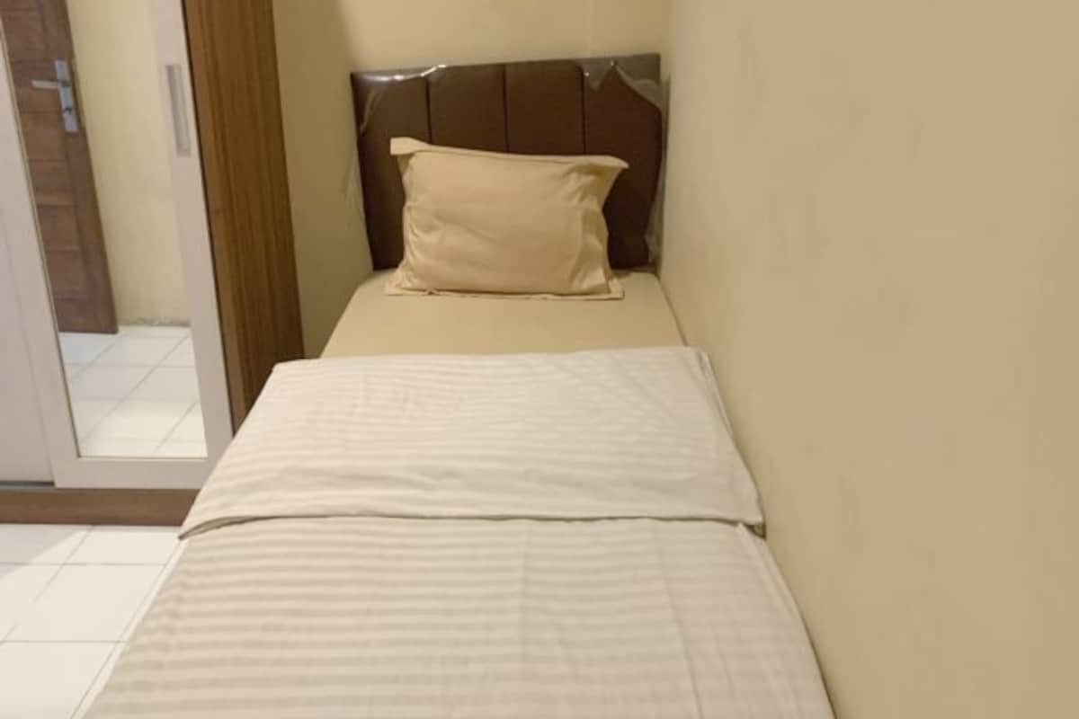 A small, single-bed room with a wooden headboard and a beige pillow.