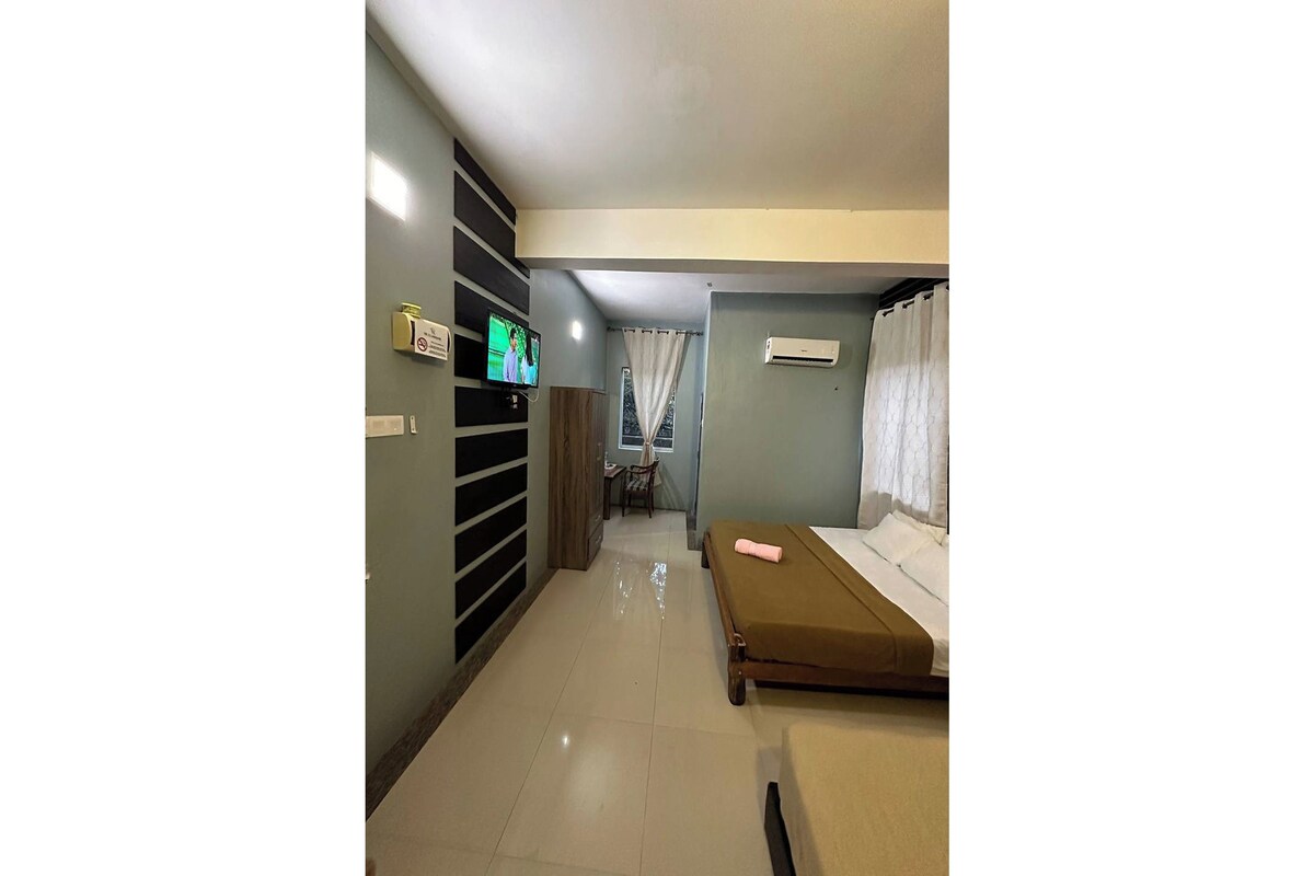A hotel room with a bed, a TV, a desk, and a window with curtains.