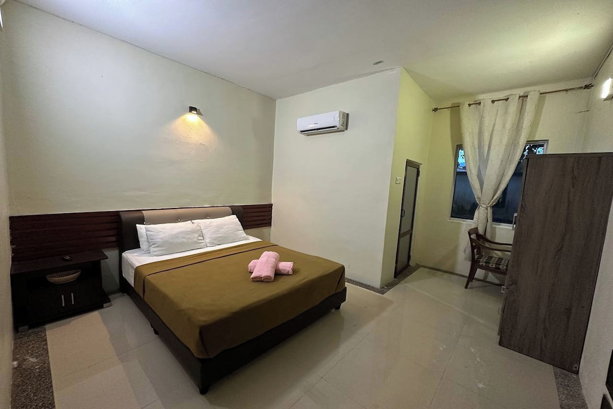 A hotel room with a bed, bedside table, and a window with curtains.