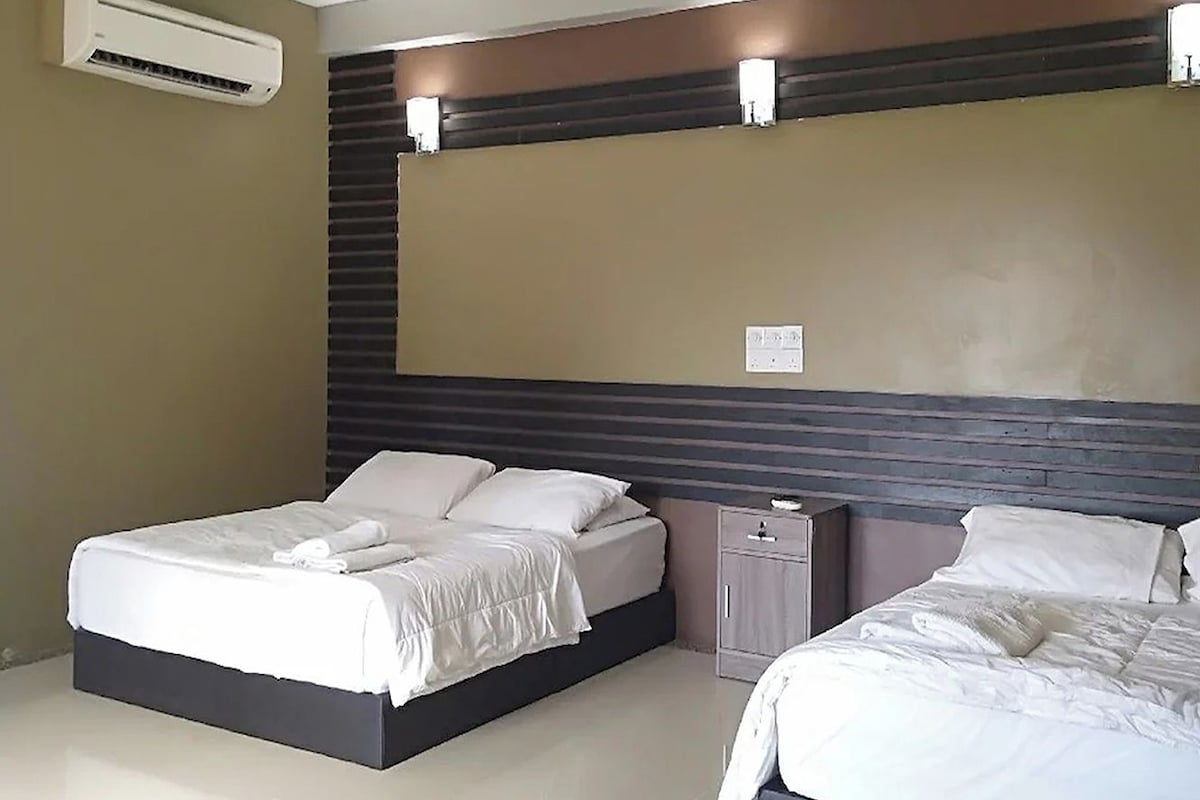 A hotel room with two beds, a wall-mounted air conditioner, and a bedside table with a lamp.