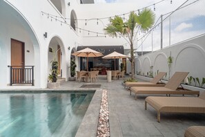 A poolside area with lounge chairs, umbrellas, and a seating area with tables and chairs. - The Simore (Tibubeneng)