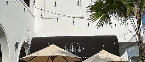 An outdoor seating area with wicker chairs and umbrellas, a palm tree, and string lights.