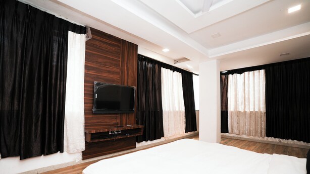 A modern hotel room with a large bed, a flat-screen TV mounted on a wooden panel, and black and white curtains. - Hotel Sai Executive Near Holy Cross Church Mahabaleshwar (Mahabaleshwar)