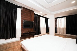 A modern hotel room with a large bed, a flat-screen TV mounted on a wooden panel, and black and white curtains. - Hotel Sai Executive Near Holy Cross Church Mahabaleshwar (Mahabaleshwar)