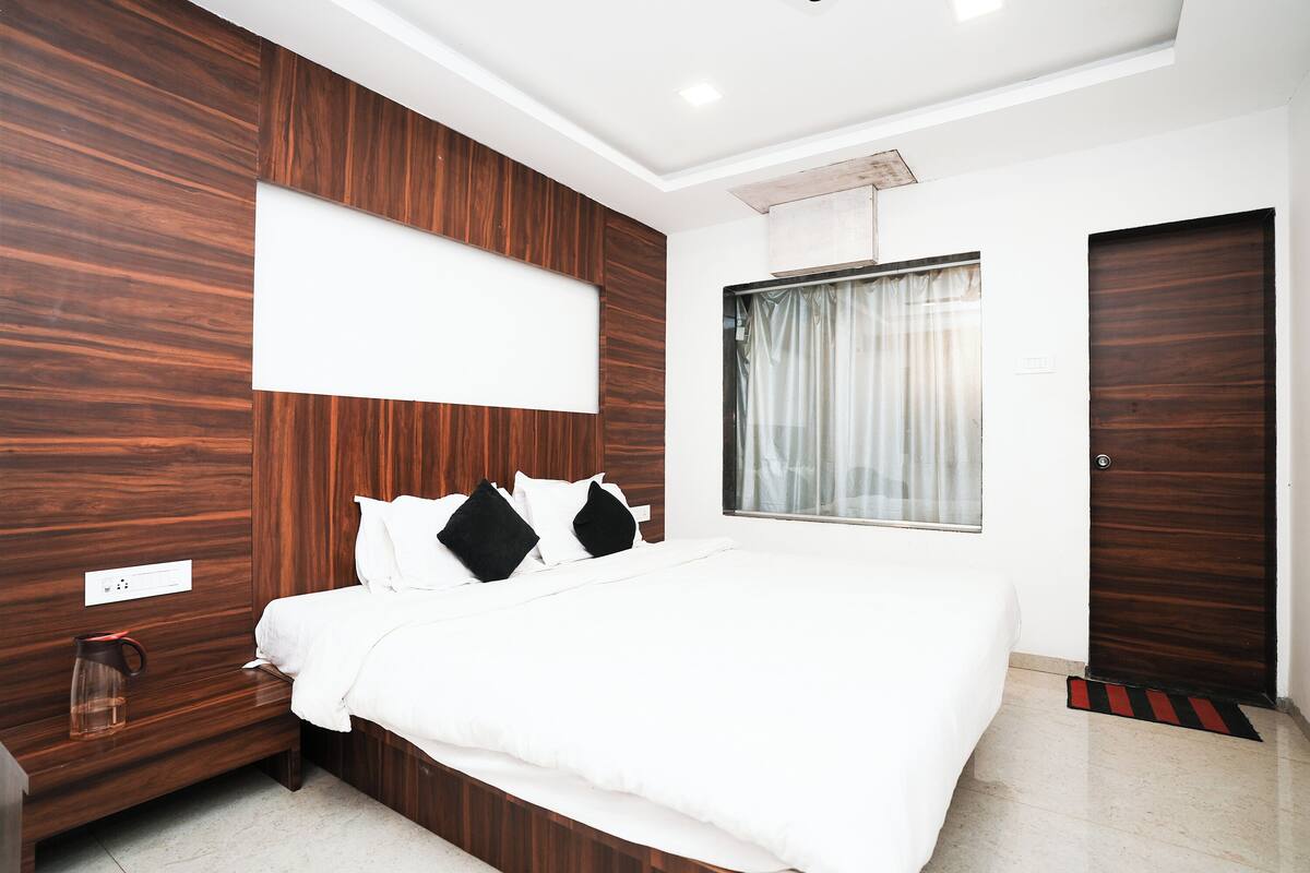A modern bedroom with a large bed, wooden paneling, a window with curtains, and a door.