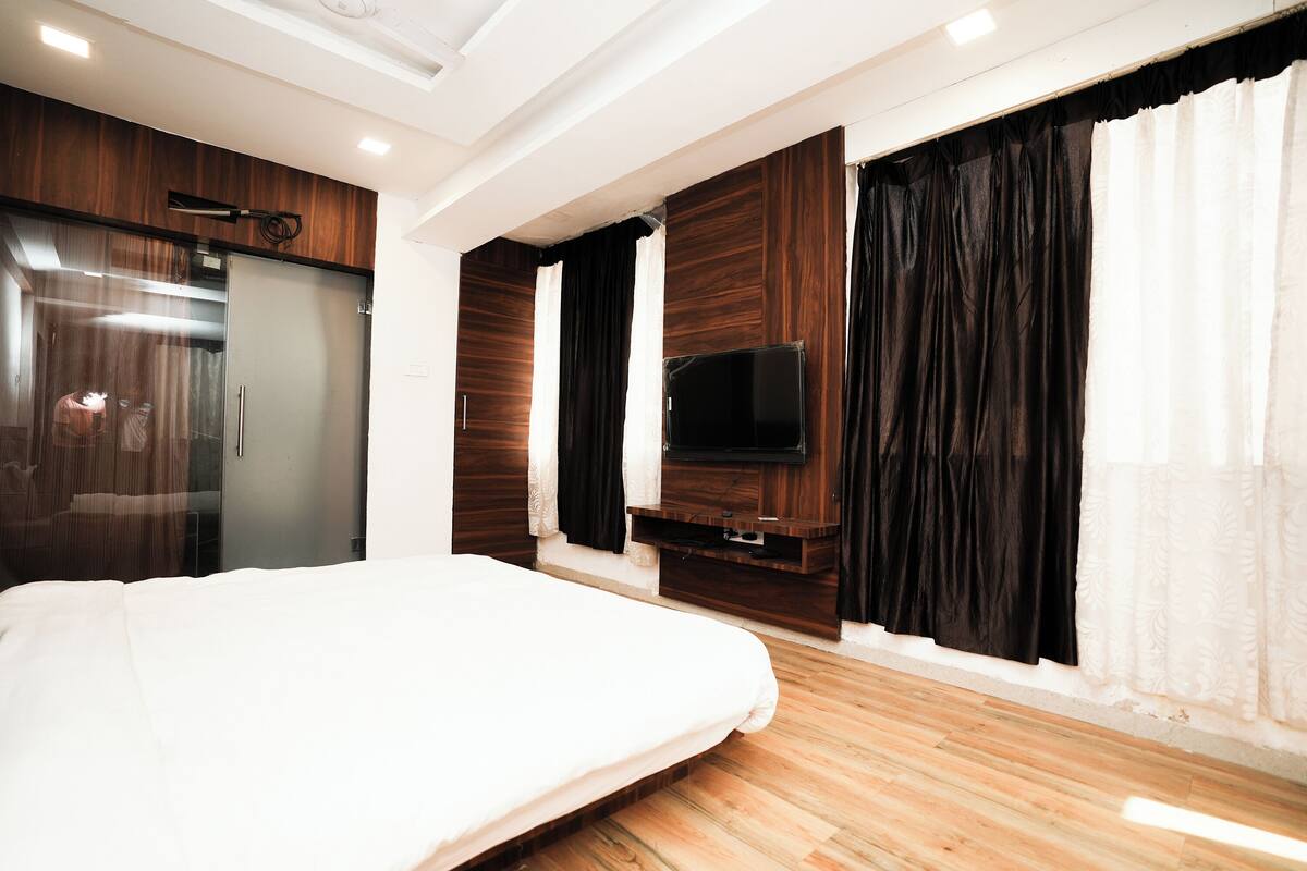A modern bedroom with a large bed, a wardrobe, a television, and a sliding door.