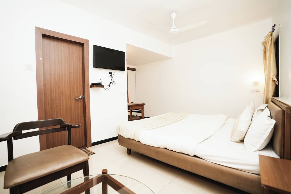 Une chambre à coucher comprenant un lit, une chaise, un téléviseur fixé au mur et un ventilateur de plafond.