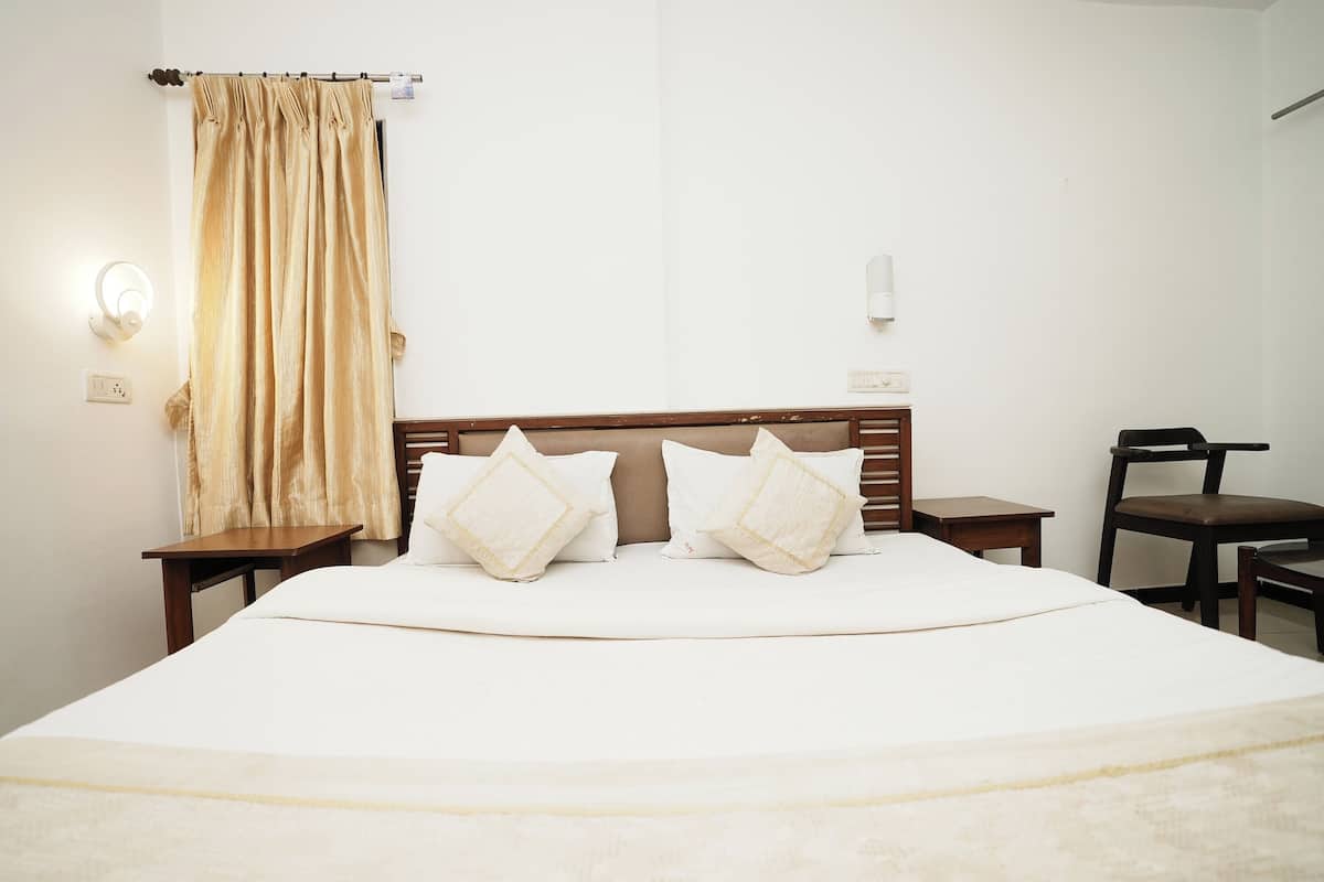 Un lit bien fait, avec du linge de lit blanc et deux coussins décoratifs, une tête de lit en bois, une table de chevet avec une lampe et une chaise placée contre le mur.