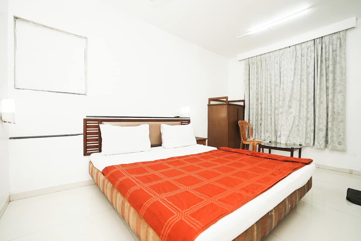 Une chambre d’hôtel avec un lit, une tête de lit en bois, une chaise, une table et une fenêtre avec des rideaux.