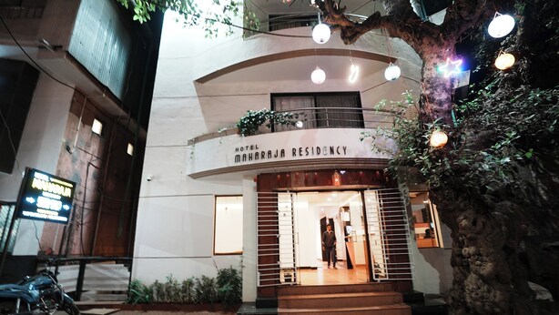 Esterno dell'Hotel Maharaja Residency, con un cartello sopra l'ingresso, una scala che conduce alla porta e un albero decorato con luci.