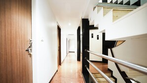 Corridoio di un hotel con una porta in legno, una ringhiera in metallo e una scala con gradini neri.