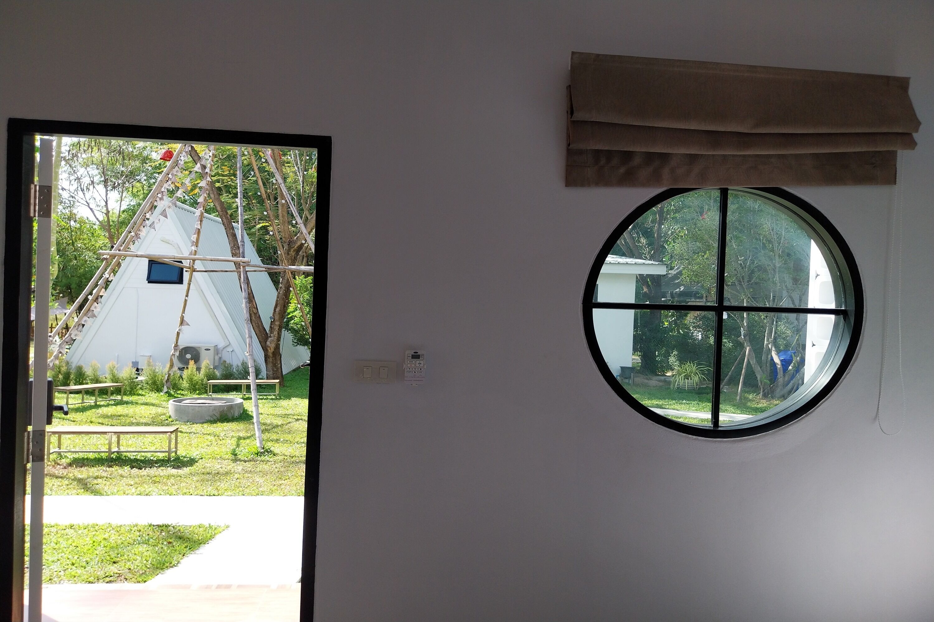 Una habitación con ventana, puerta y vistas a un espacio exterior con una tienda de campaña y árboles.