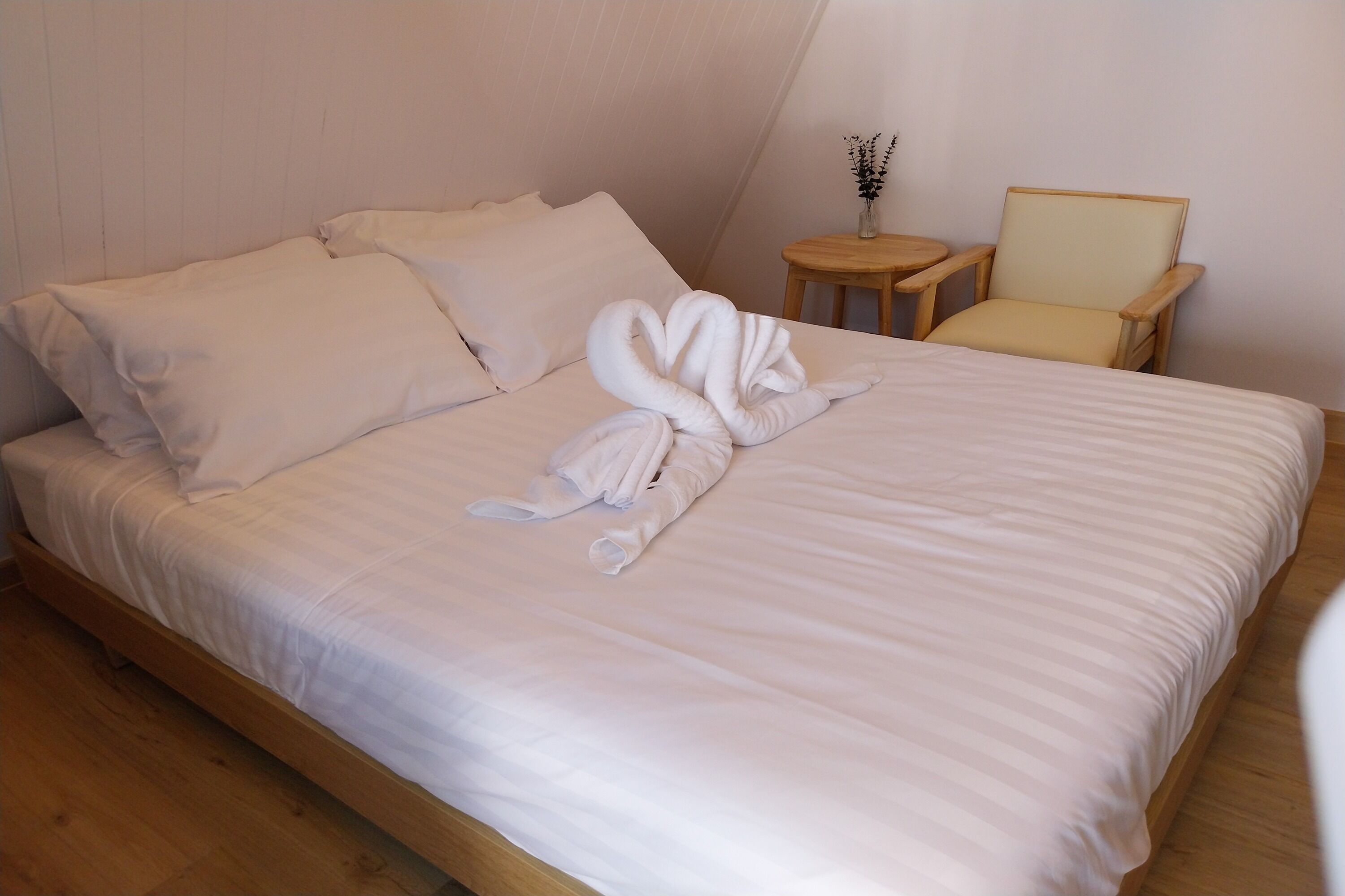 A neatly made bed with white linens and a towel arranged in a swan shape.