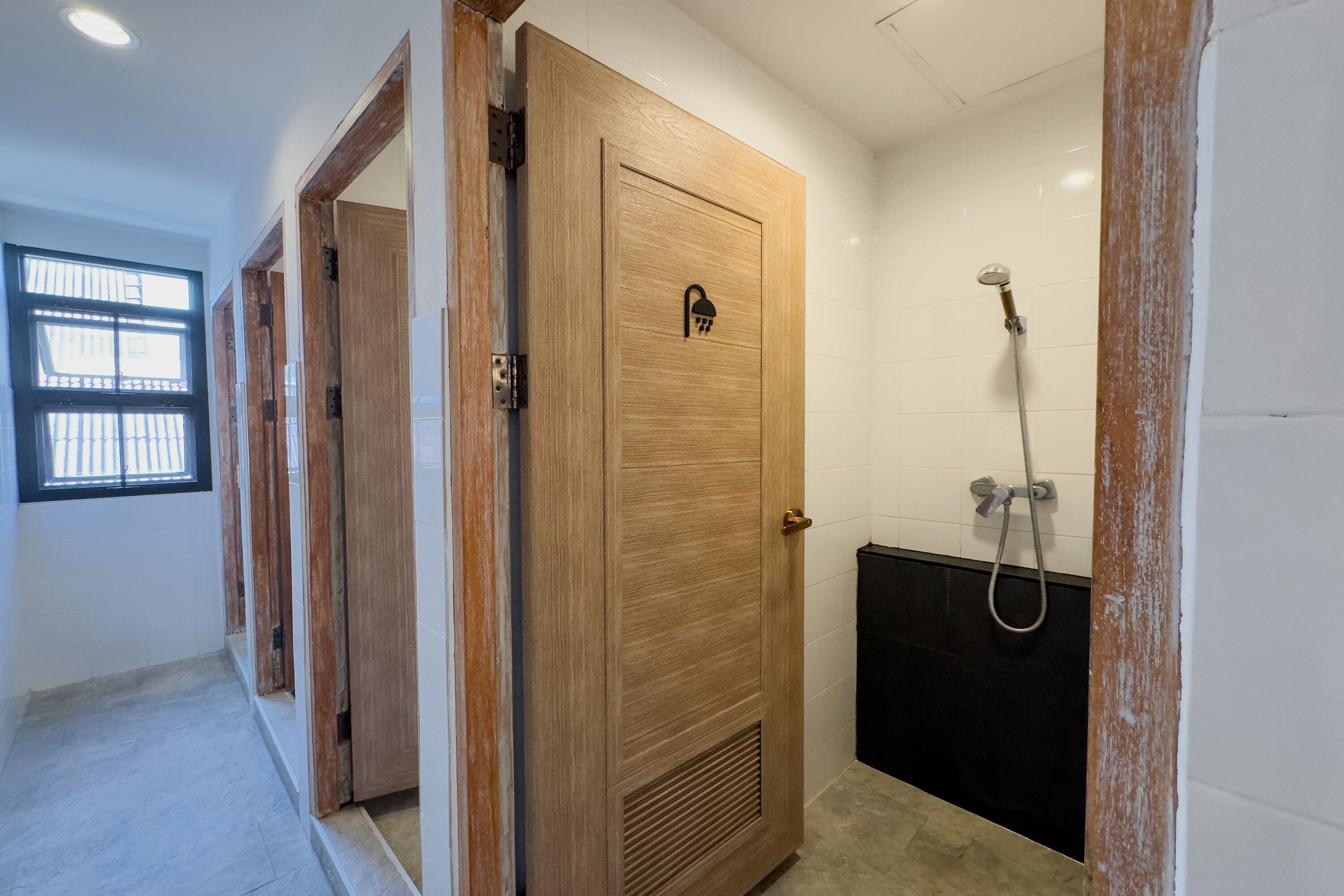 A bathroom with a wooden door, a shower, and a window with bars.