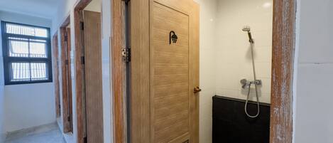 A bathroom with a wooden door, a shower, and a window with bars.