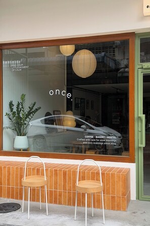 Ein Schaufenster mit großen Auslagen, in denen ein Auto und ein Schild mit der Aufschrift 'once COFFEE . BAKEY . HOSTEL' zu sehen sind.
