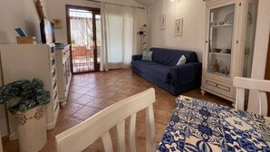 A living room with a sofa, a cabinet, a dining table, and a view through a door. - VILLA ELENA PRIVATE POOL (Sardegna)