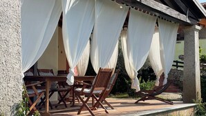 A covered outdoor seating area with a table and chairs, a hammock, and a stone pillar. - VILLA ELENA PRIVATE POOL (Sardegna)