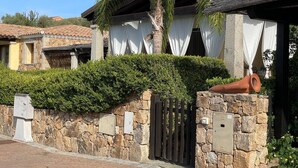 A stone-walled building with a gated entrance, a palm tree, and a tiled roof. - VILLA ELENA PRIVATE POOL (Sardegna)