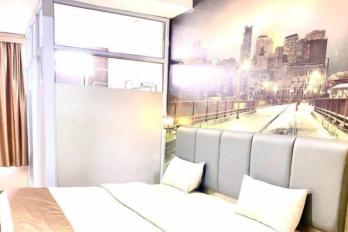 A modern hotel room with a large bed, a cityscape mural on the wall, and a window with curtains.