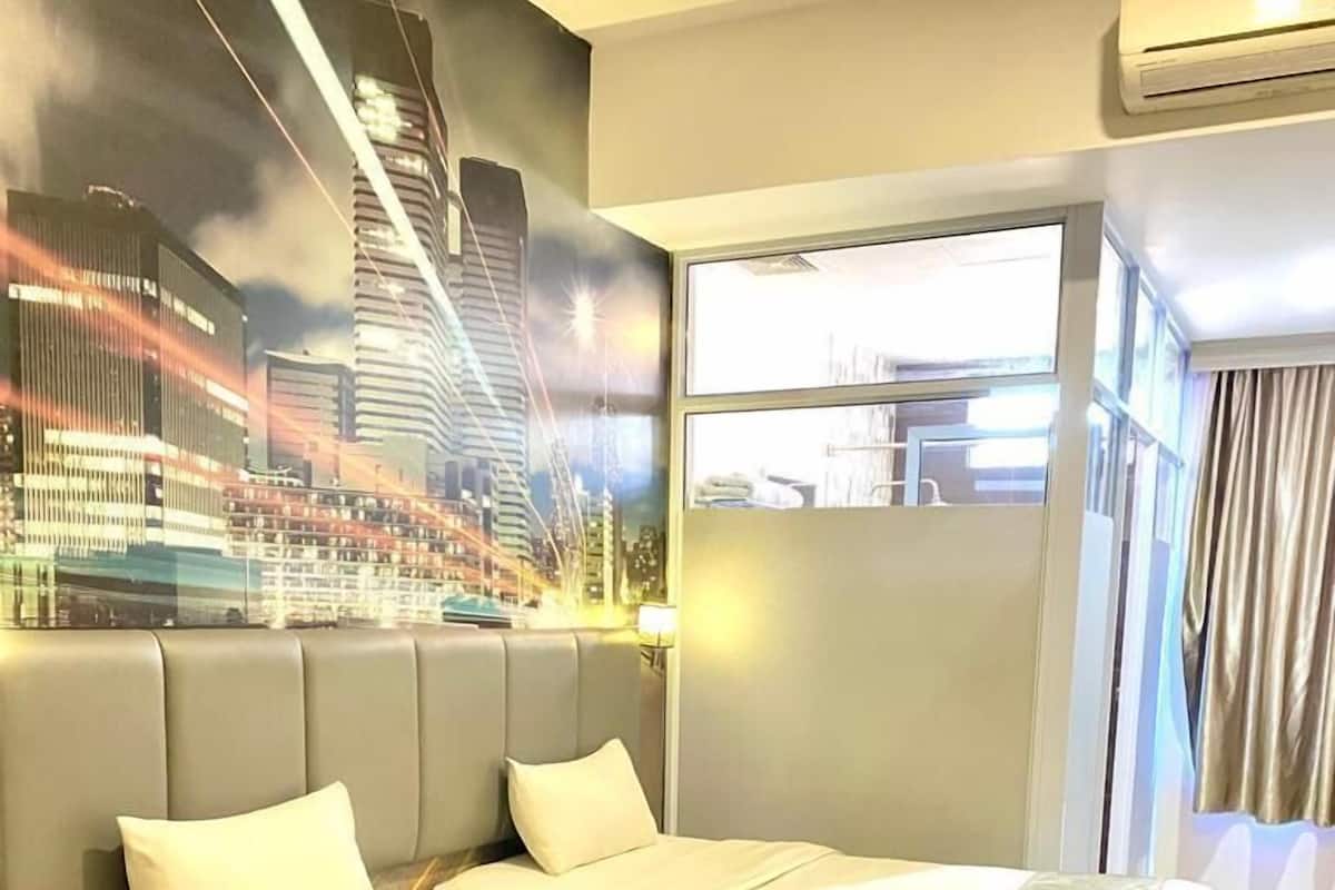 A hotel room with a large bed, a cityscape mural, and a view of the city through the window.