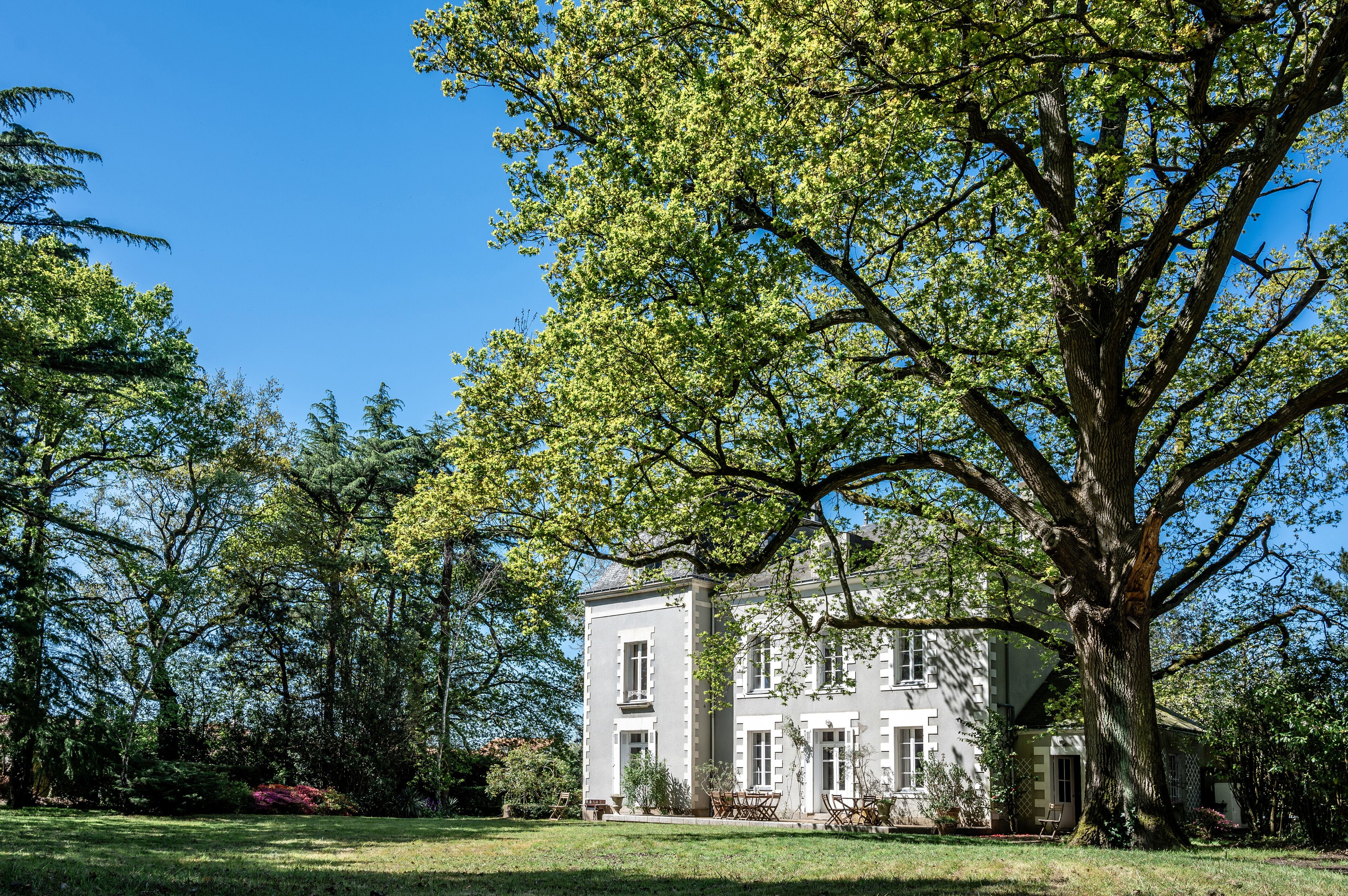 Un grand bâtiment historique à la façade symétrique, entouré d’une végétation luxuriante et d’arbres majestueux.