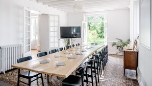 A long conference table with chairs, a television, and a view of greenery outside.