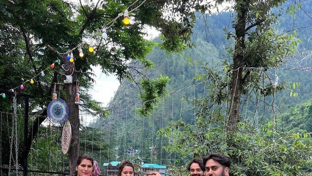 A group of people seated around a round table outdoors with a mountainous backdrop. - Namste Kasol Camps (Bhuntar)