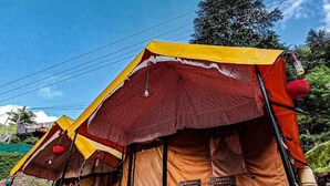 A series of tents with a simple layout, including seating and a table, set against a backdrop of greenery and a clear sky. - Namste Kasol Camps (Bhuntar)
