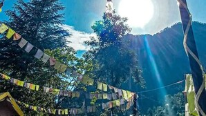 A clear sky with sunlight, a mountain, and a structure with colorful flags. - Namste Kasol Camps (Bhuntar)